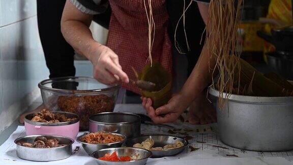 一位年长的亚洲华人妇女在她的厨房里准备粽子把配料包好为端午节做准备