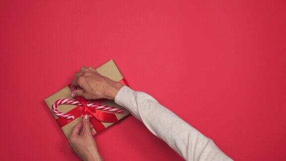 双手将装有棒棒糖的圣诞礼盒放在红色的平板上