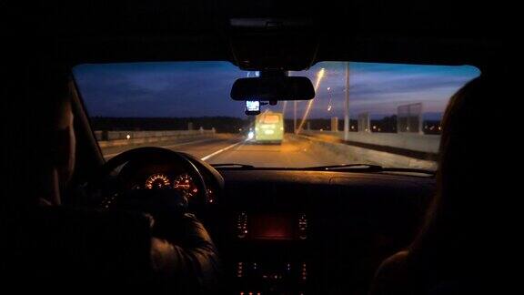 年轻夫妇坐在SUV车的前座上在空旷的路上行驶男人和女人在晚上乘坐现代汽车女朋友和男朋友晚上在高速公路上开着汽车
