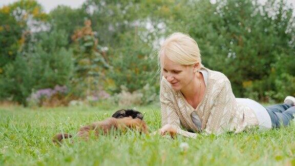 一位妇女躺在草地上和她院子里有趣的小狗玩耍