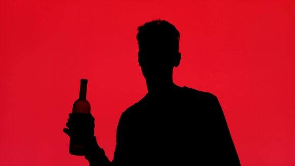一个男人在红色背景上喝着一瓶酒的剪影