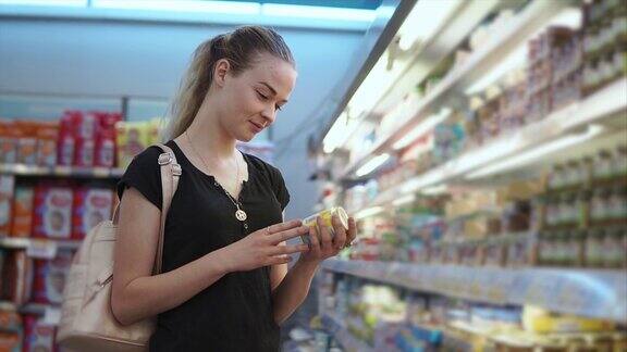 年轻的母亲正在看商店里一罐婴儿酱标签上的文字