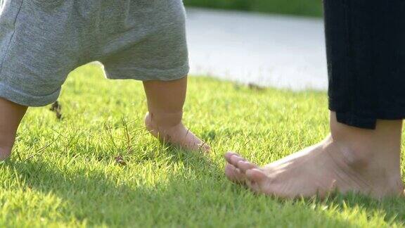 小男孩学着在绿草地上走路迈出他的第一步妈妈牵着他的手