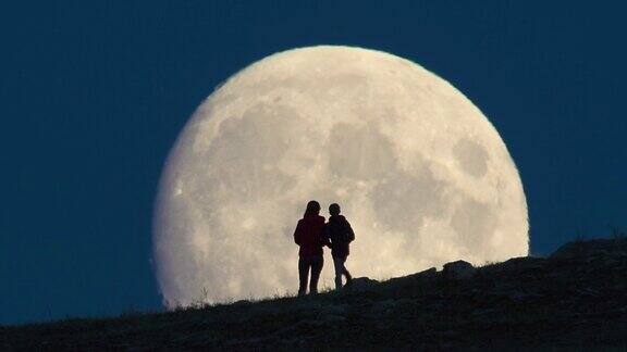 两个人站在巨大的月亮背景下的剪影