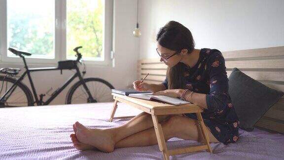 女学生坐在床上用铅笔做笔记