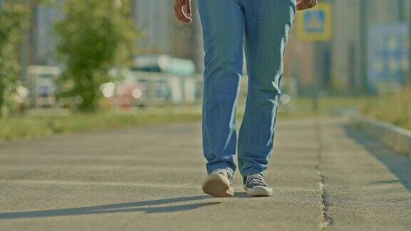 一个穿着运动鞋的男人沿着路走一个穿着牛仔裤的男人的腿走在城市的街道上从下面看4kProRes