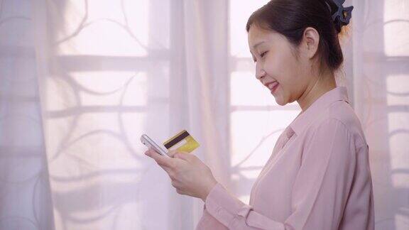 快乐的年轻女性持有银行信用卡在移动应用程序在线支付