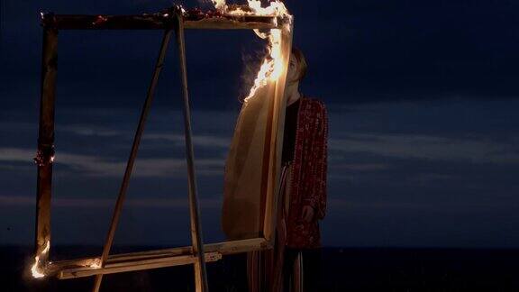 黄昏时分年轻的艺术家站在一个燃烧着的画架前