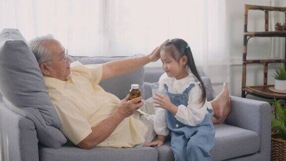 孙女给爷爷拿来了药和水让爷爷坐在客厅的沙发上吃