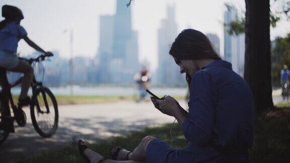 夏天坐在公园里玩智能手机的快乐女人迷人的女性花闲暇时间在市中心