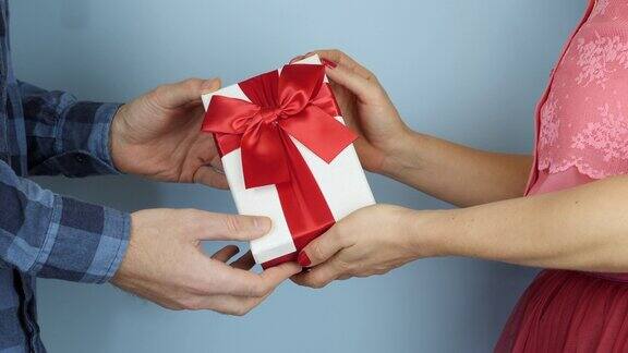 男人正在接受生日或情人节的礼物和红色的丝带蝴蝶结女性手里拿着系着蝴蝶结的礼盒送给男性特写节日的礼物