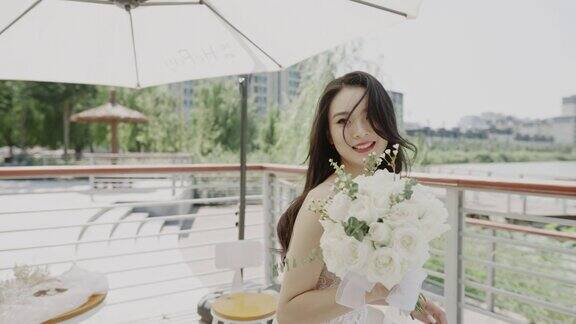 一位年轻漂亮的亚洲女子身着婚纱手持一束鲜花坐在婚礼现场的遮阳伞下