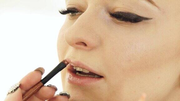 手化妆艺术家与化妆笔画嘴唇在女人的脸上唇妆合上