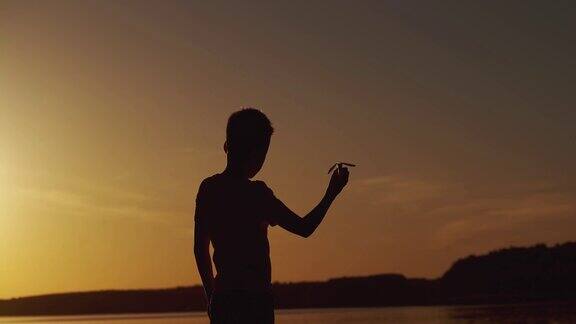 小男孩独自坐在河边的剪影在夕阳的背景