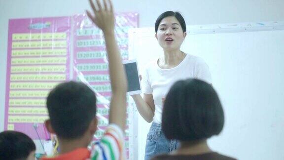 一群学校的亚洲孩子坐在教室里举起手臂回答老师的问题回归学校和教育理念慢镜头