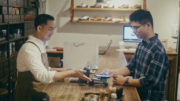 亚洲男人在男士精品店用手机付款(慢镜头)