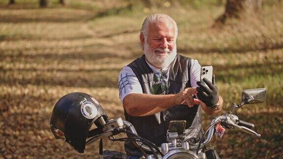 高级白人男性骑摩托车的人坐在摩托车上用手机视频通话