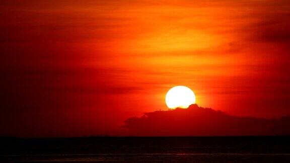 日落在红橙色的天空上在浅橙色的云和黑暗的海时间流逝