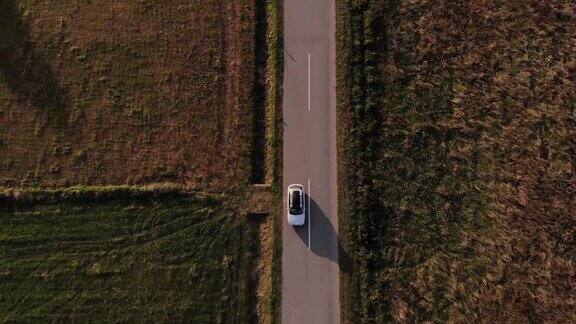 在一个金色的夏日夕阳下一辆白色的汽车行驶在空旷的乡村道路上