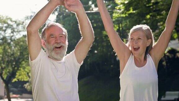 老人和女人在公园里做运动他们高高举起手微笑着跑着