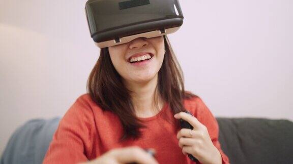 亚洲女性戴着虚拟现实眼镜坐在家里的沙发上玩360度游戏Metaverse乐趣与vr耳机和新技术
