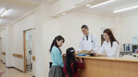 医生和护士在医生办公室的接待处与母亲和女儿交谈