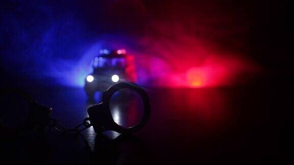 警方夜间突袭你将被逮捕手铐的剪影与警车在后面与闪烁的红色和蓝色警灯在雾蒙蒙的背景滑块拍摄