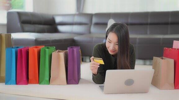 年轻的亚洲女性使用笔记本电脑或手机或信用卡在网上购物