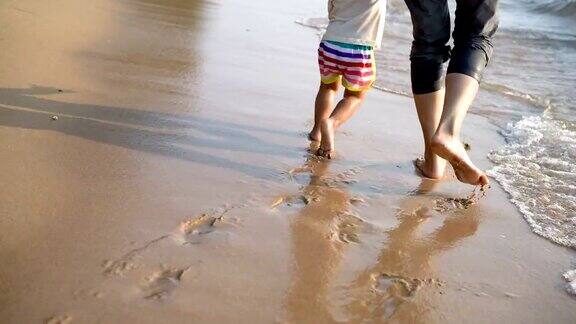 2岁的亚洲男婴和母亲在海滩上散步