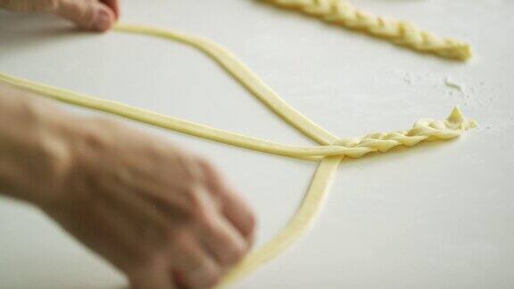 一个女人的手编织在一起的面团条在一个白色的桌子上烤
