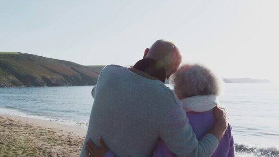 在冬季海滩度假沿着海岸线散步的热爱活跃的老年夫妇的后视图