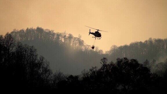 在森林大火中直升飞机的剪影和消防人员的喷水