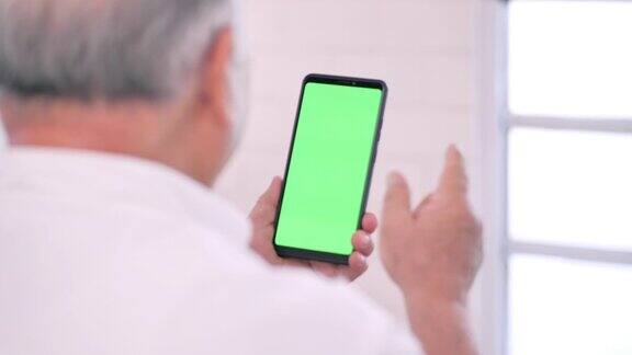 亚洲老爷爷在家看智能手机绿屏用智能手机进行视频会议家庭高级卫生技术医疗退休电子学习医学和保健绿色屏幕手持智能手机