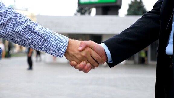 商业握手与模糊的城市背景两个不认识的商人在城市环境中互相问候伙伴们在外面握手同事们在户外见面握手特写慢动作侧视图