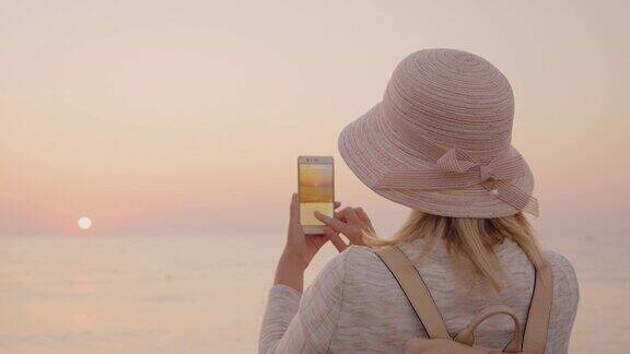 一个穿着粉红色衣服的成年女孩在海边欣赏日出用手机拍了一张照片