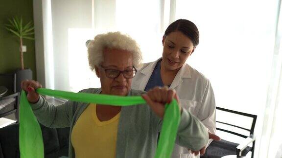 理疗师帮助老年妇女在家里用阻力带做练习