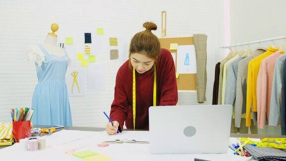 亚洲女性时装设计师使用笔记本电脑而工作在她的办公桌在她的工作室工作地点亚洲小型企业