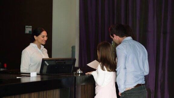 友好的接待员在豪华酒店为幸福家庭登记入住