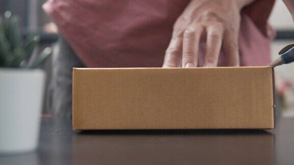 男子使用锋利的刀切割和打开盒子包装从他的网上购物