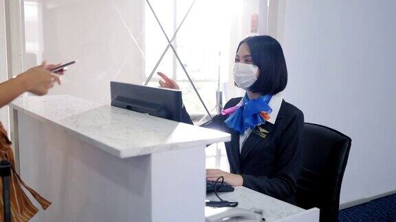 美丽的亚洲女性地勤人员带着防护口罩在机场值机柜台为女性乘客办理登机手续遵守航班规则在COVID-19期间旅行