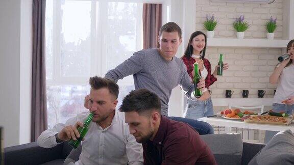 在家里朋友们坐在沙发上喝着啤酒瓶玩着电子游戏