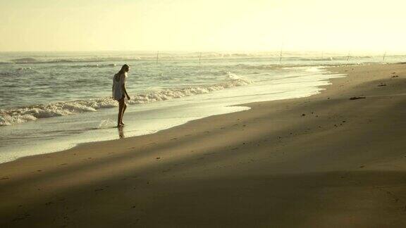 一个美丽的女人沿着海滩散步的慢动作镜头这是日落和海浪很大