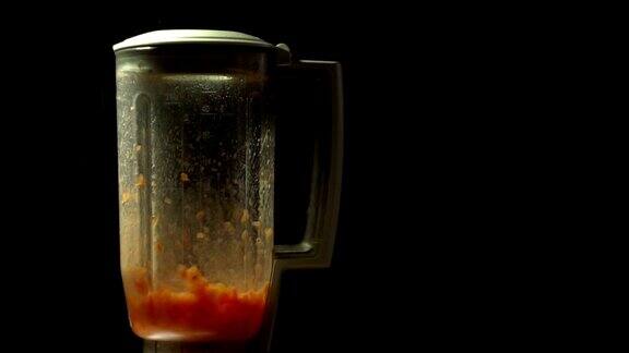 在黑色背景下用慢动作在搅拌机里切番茄