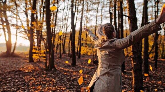 MS超级慢镜头无忧无虑的年轻女子在森林里的金秋落叶中嬉戏