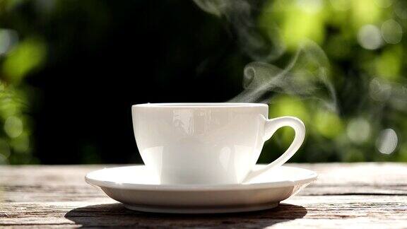 咖啡杯与自然蒸汽烟热饮特写热咖啡杯在花园户外背景的早晨阳光下逼真的自然蒸汽升起烟雾4K热饮概念