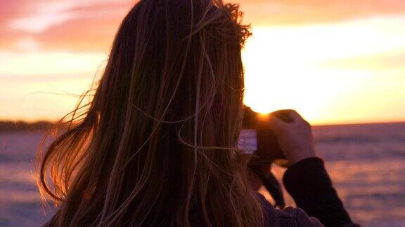 特写:不知名的女摄影师拍摄日落从一个风景优美的海滩