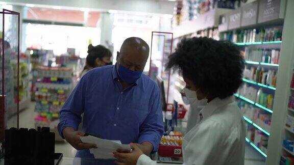 年轻的药剂师在药店帮一位年长的人戴着口罩