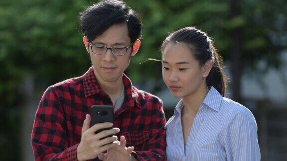 年轻的亚洲夫妇一起在户外使用电话