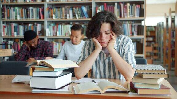 疲惫的少年摸着脸在大学图书馆的书桌前学习