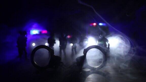 警方夜间突袭你将被逮捕手铐的轮廓和警车在后面在雾蒙蒙的背景下红色和蓝色警灯闪烁有选择性的重点
